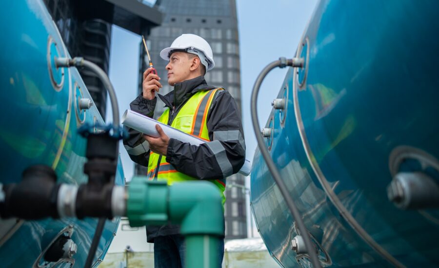 Engineer inspects water heater pump system and hot water tank on industrial roof