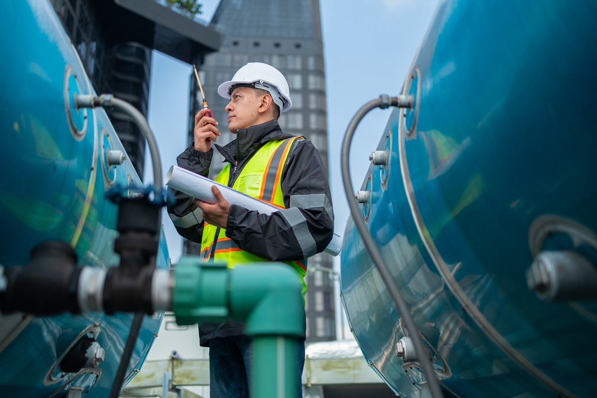 Engineer inspects water heater pump system and hot water tank on industrial roof